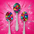 Three silver blinged-out ice cream scoop spoons with colorful jewel-toned beads on a hot pink glitter background
